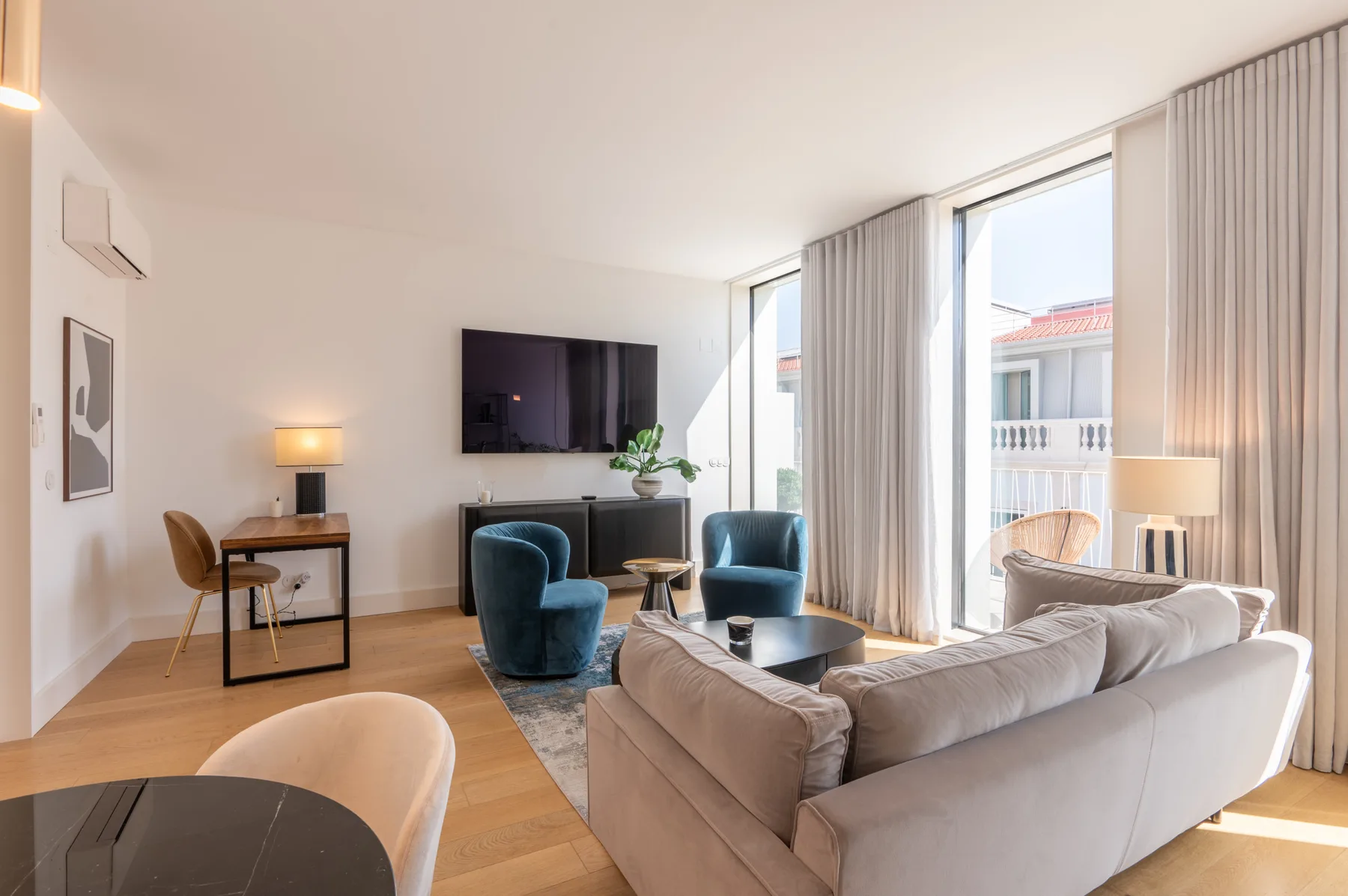 A bright living room with seating, a television, and large windows.