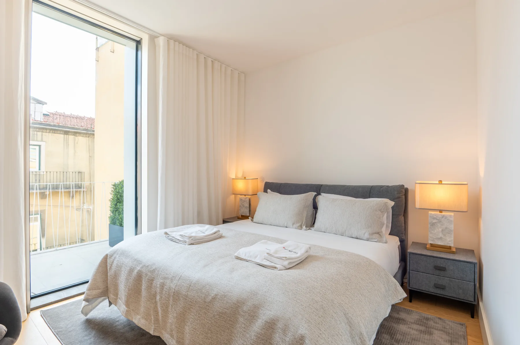 Un dormitorio con una cama bien hecha junto a una gran puerta de vidrio al balcón.