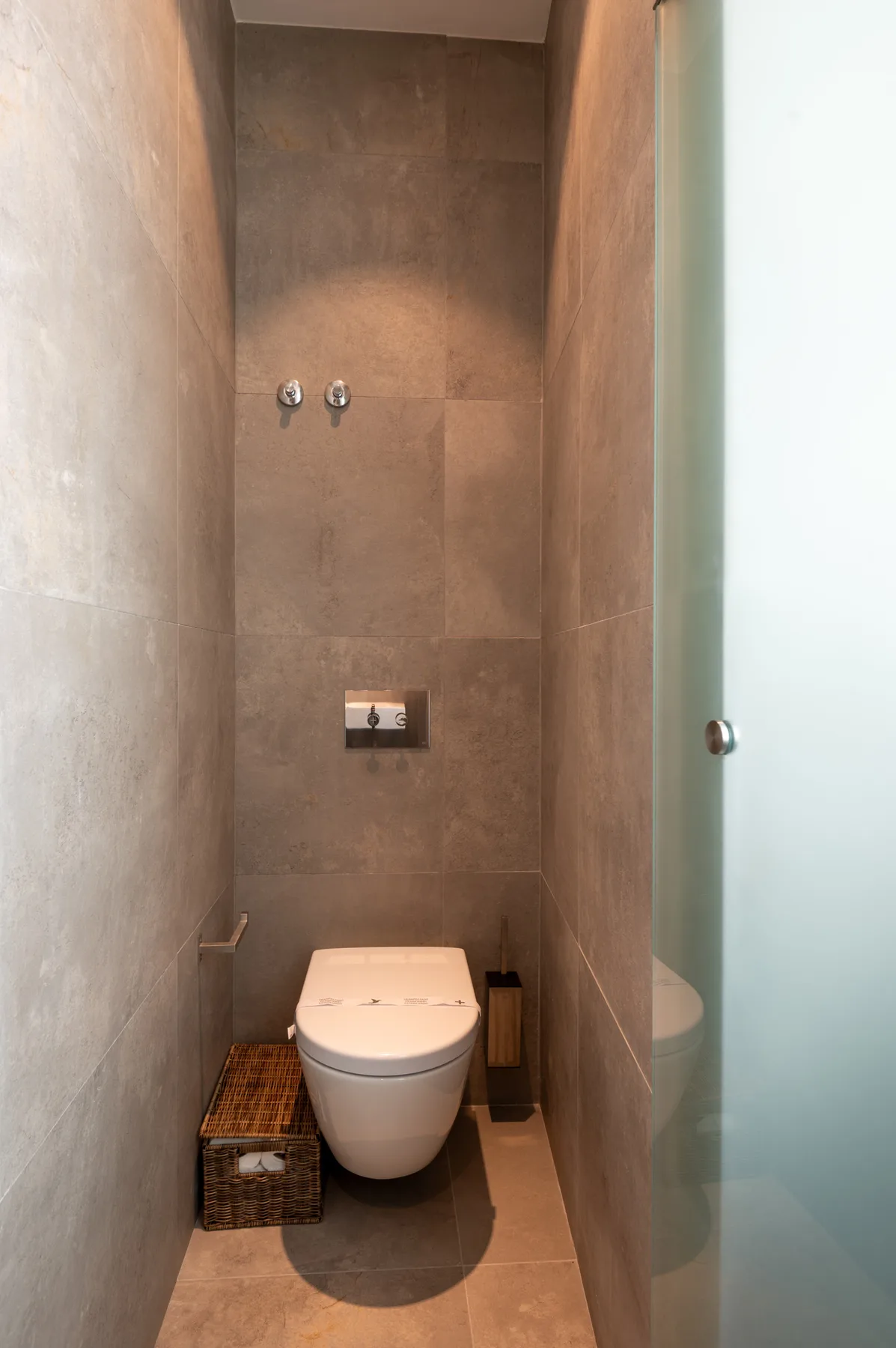 A tiled bathroom with a toilet and wall-mounted controls.
