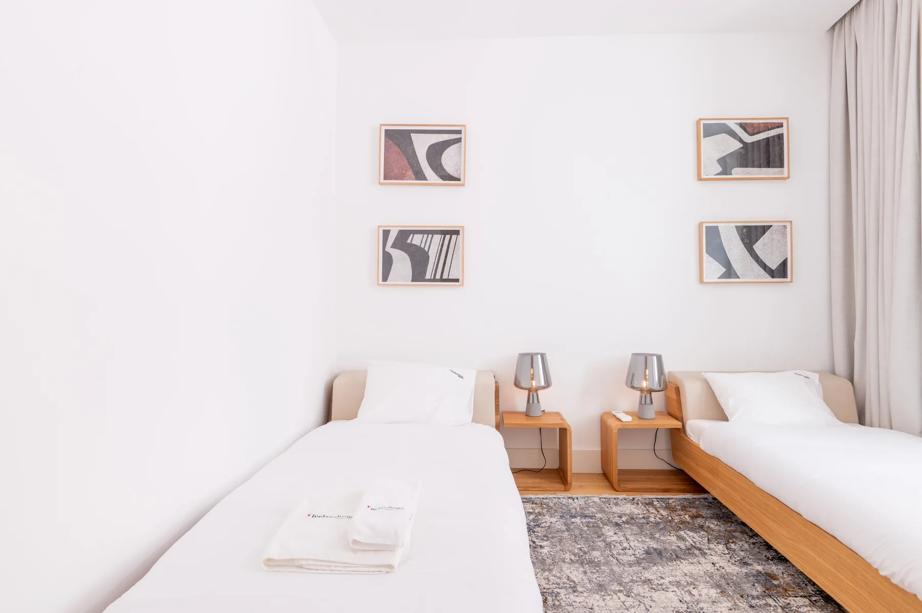 Un dormitorio luminoso con dos camas, mesitas de noche y arte abstracto en la pared.