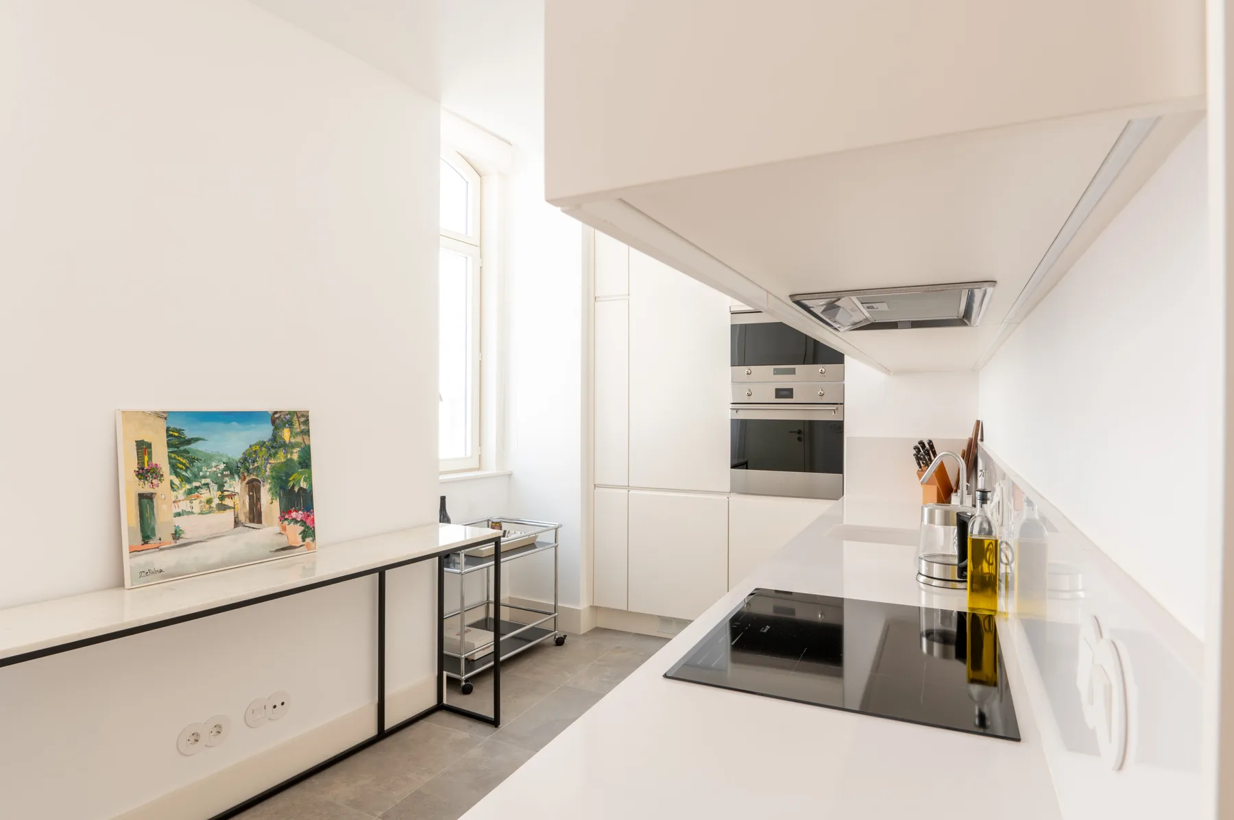 A bright modern kitchen with white cabinets, an oven, and a cooktop.