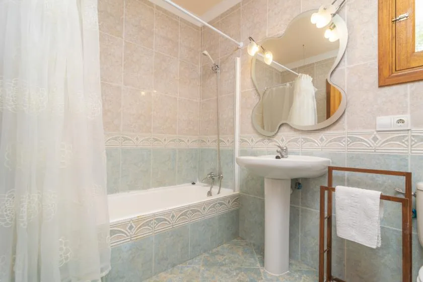 Un baño alicatado con bañera, cortina de ducha y lavabo con pedestal.