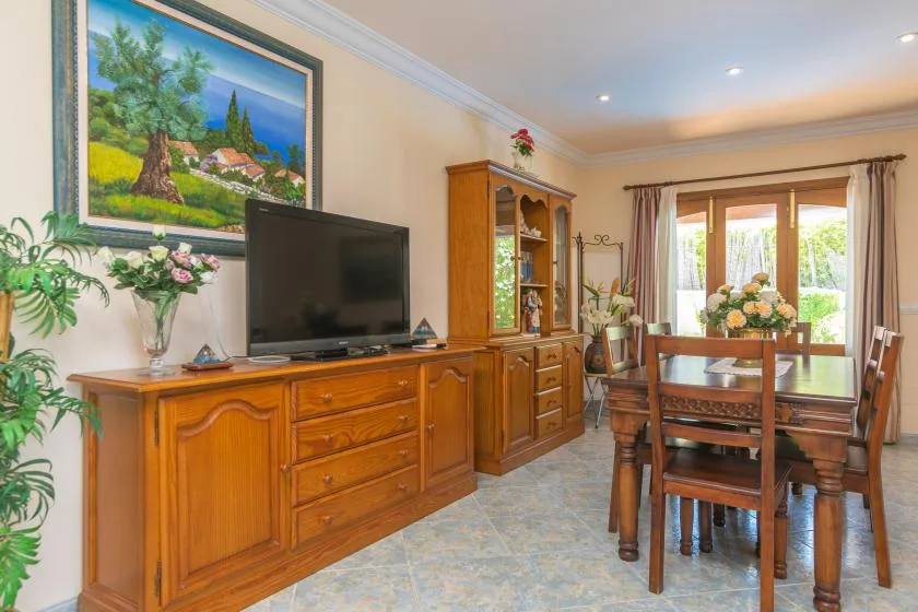 Una zona de comedor y estar con una mesa de madera, televisor y aparador.