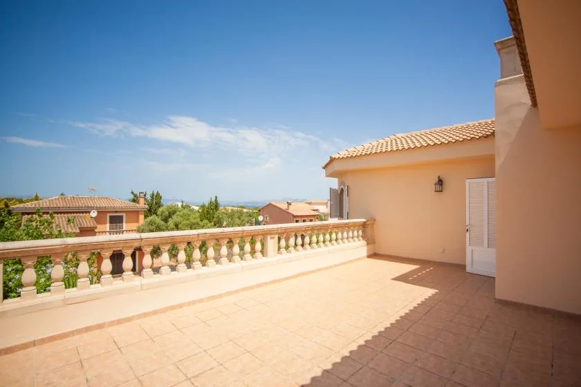 Una terraza soleada con suelo de baldosas y una balaustrada baja da a casas cercanas.