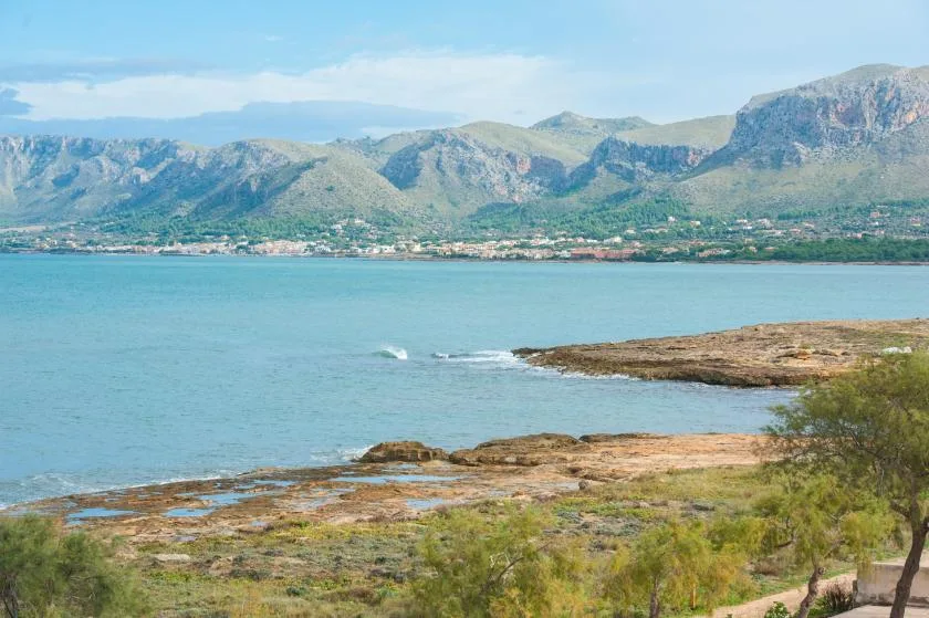 Una bahía costera con una orilla rocosa baja y montañas al otro lado del agua.