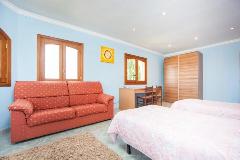 Un dormitorio azul con un sofá rojo, una cama y un armario de madera.