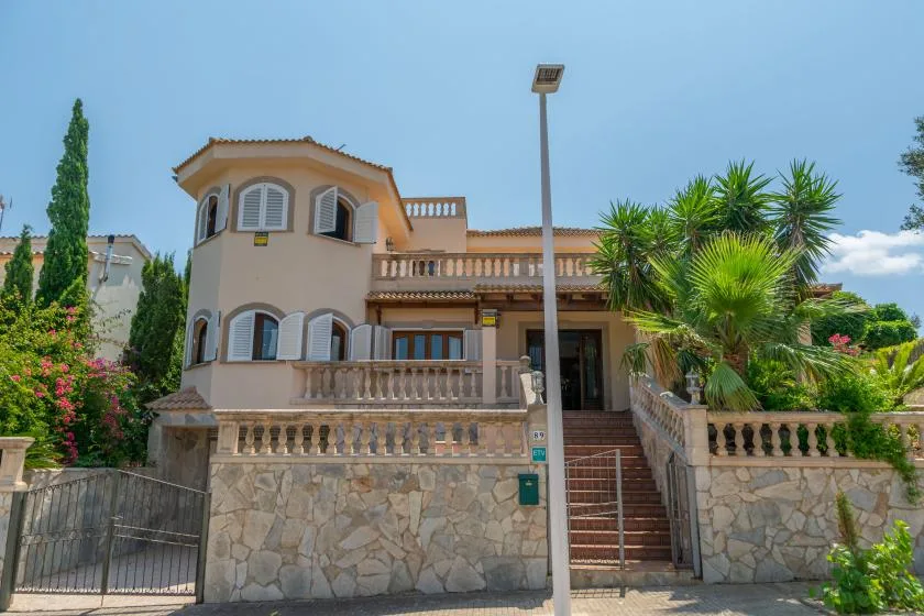 Una casa de estuco se alza tras un muro de piedra, con palmeras junto a la entrada.