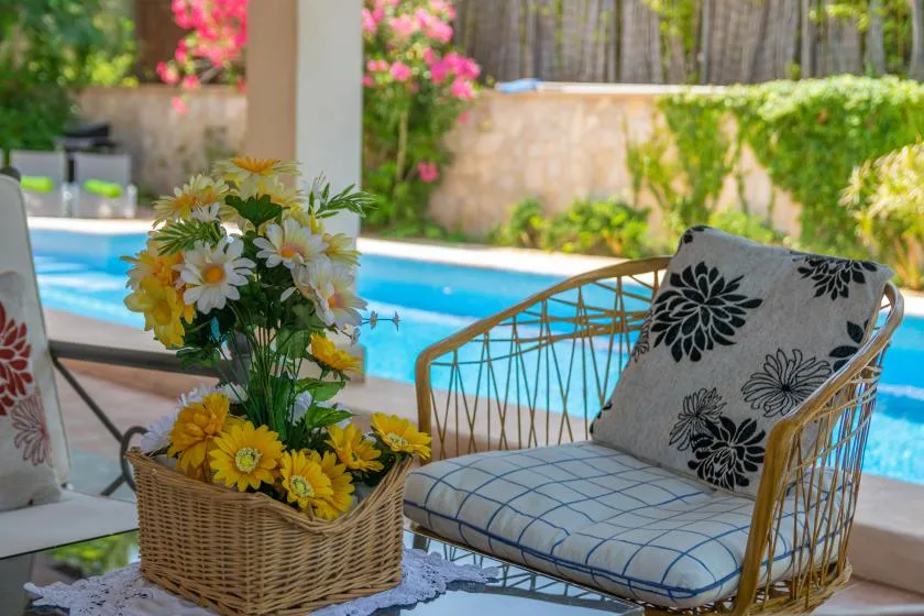 Asientos en un patio junto a una piscina, con una cesta de flores sobre la mesa.
