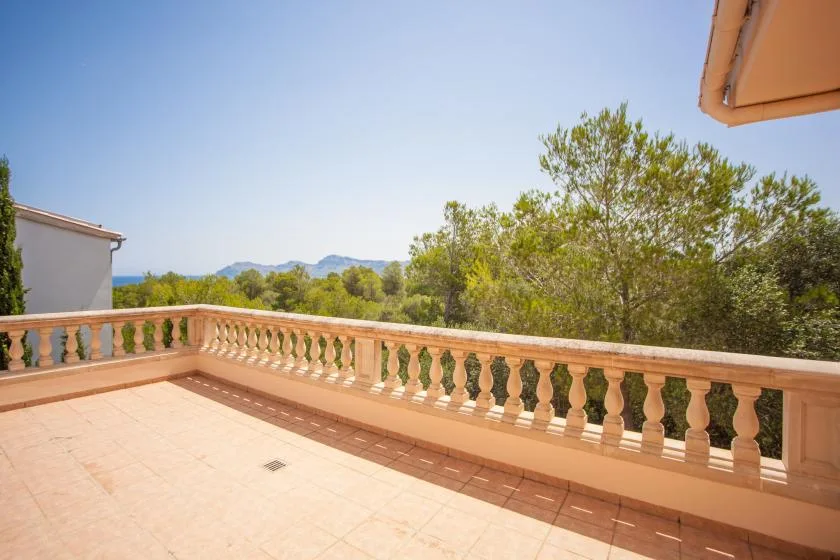 Una terraza exterior soleada con suelo de baldosas y una balaustrada frente a los árboles.
