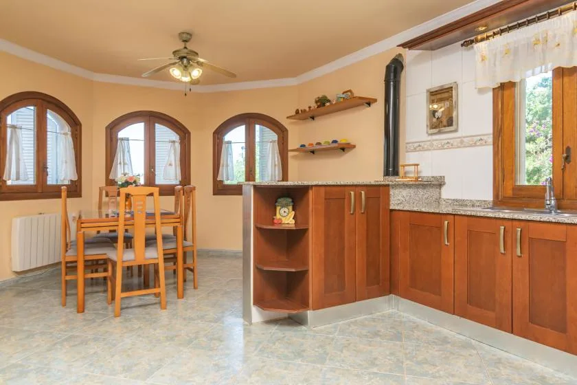 Cocina y comedor con muebles de madera, una mesa y ventanas arqueadas.
