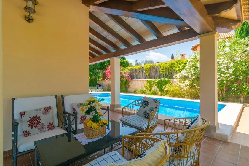 Un patio cubierto con asientos al aire libre da a una piscina y un jardín.