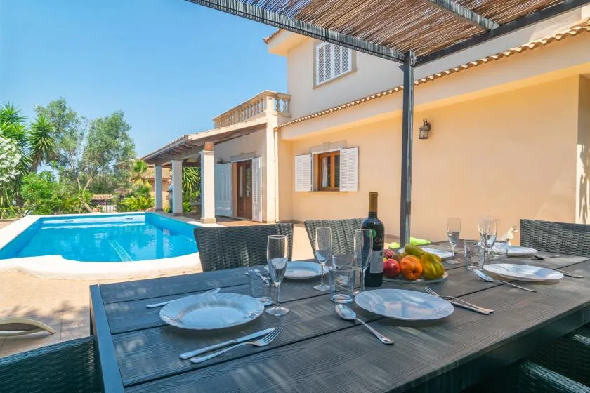 Una mesa de comedor al aire libre está junto a una piscina y una casa.