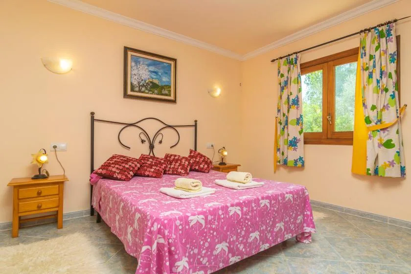 Un dormitorio con una cama doble cubierta con ropa de cama floral rosa junto a una ventana con cortinas.