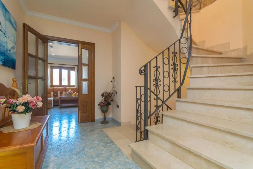 Una entrada interior con una escalera y una zona de estar visible a través de la puerta.