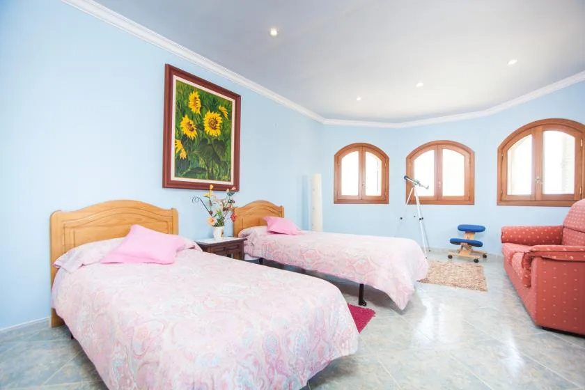 Un dormitorio azul claro con dos camas y ventanas arqueadas.