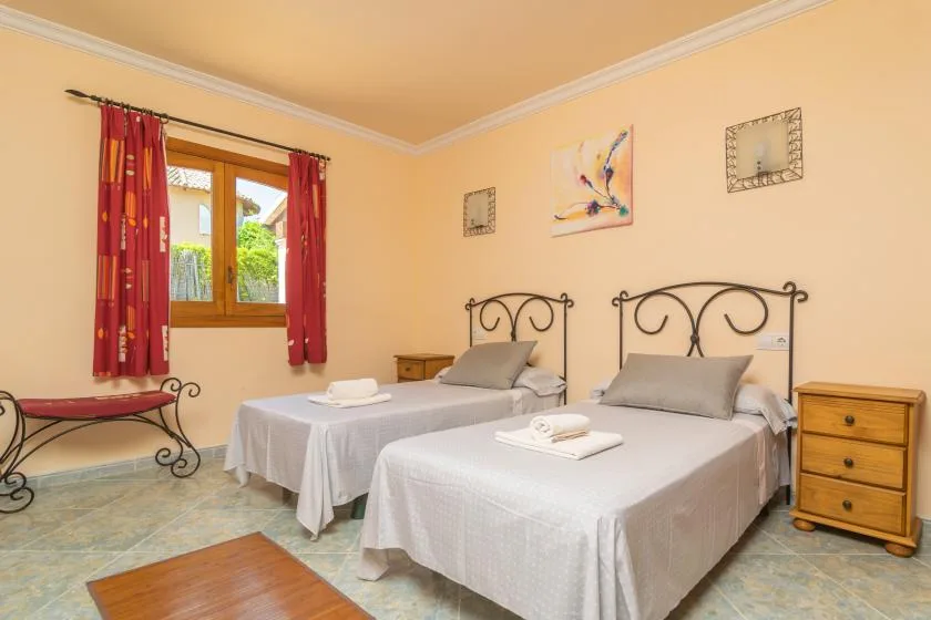 Un dormitorio con dos camas, una ventana y cortinas rojas.