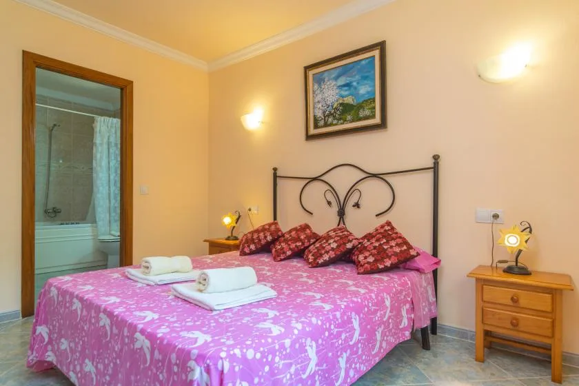 Un dormitorio con una colcha rosa, almohadas estampadas y un cuadro enmarcado sobre la cama.