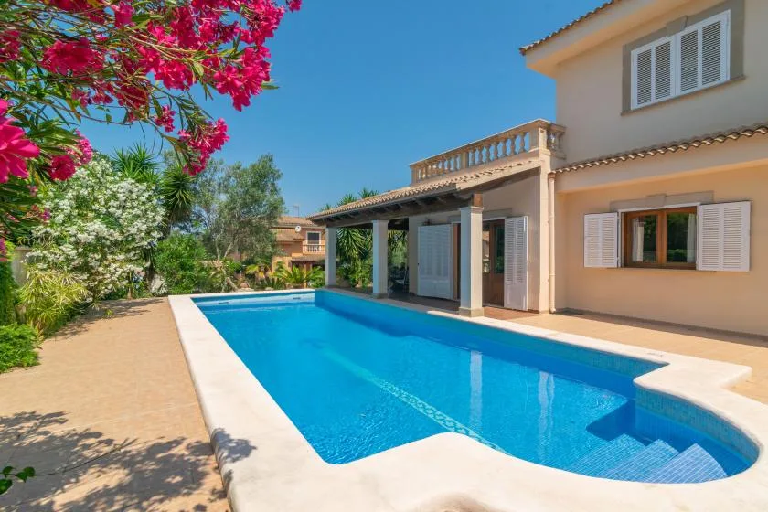 Una piscina junto a una casa, con árboles en flor junto al patio.