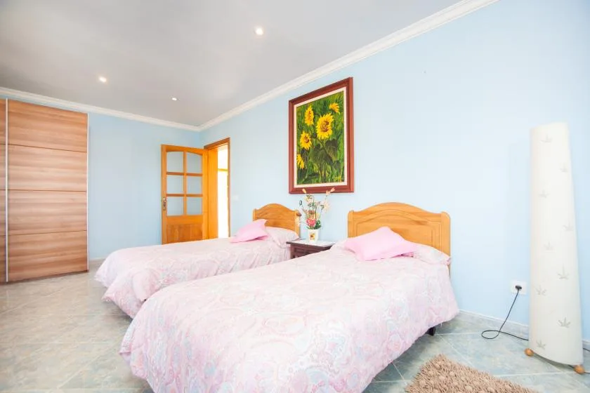 Un dormitorio con dos camas, ropa de cama clara y un cuadro floral enmarcado.