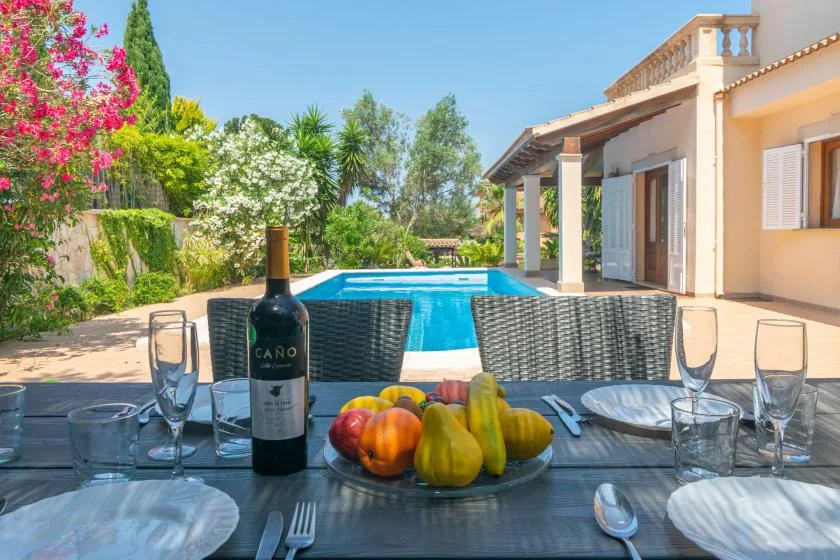 Una mesa con fruta da a una piscina junto a una casa.
