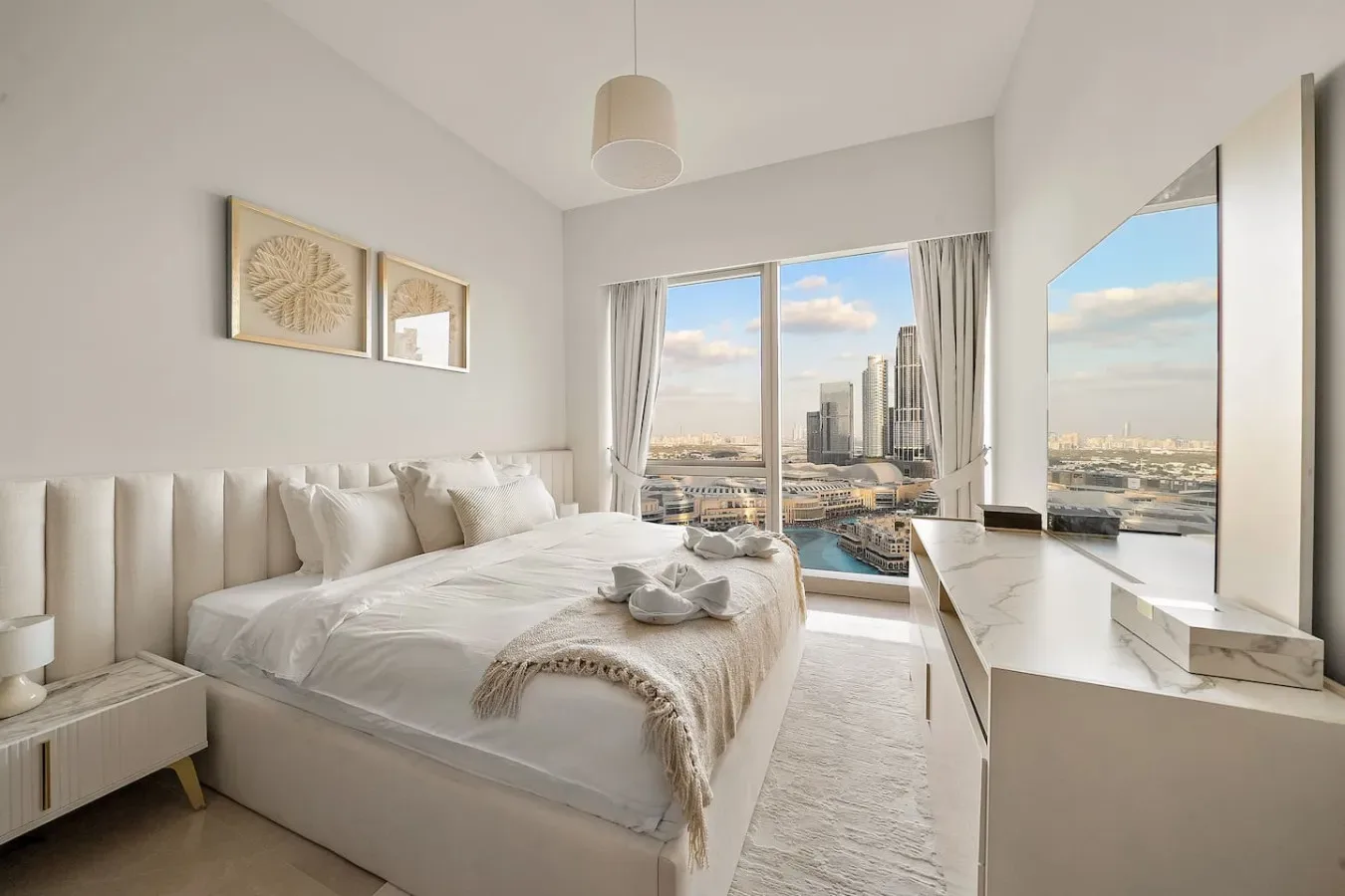 Un dormitorio luminoso con una cama grande junto a ventanas de suelo a techo con vistas a la ciudad.