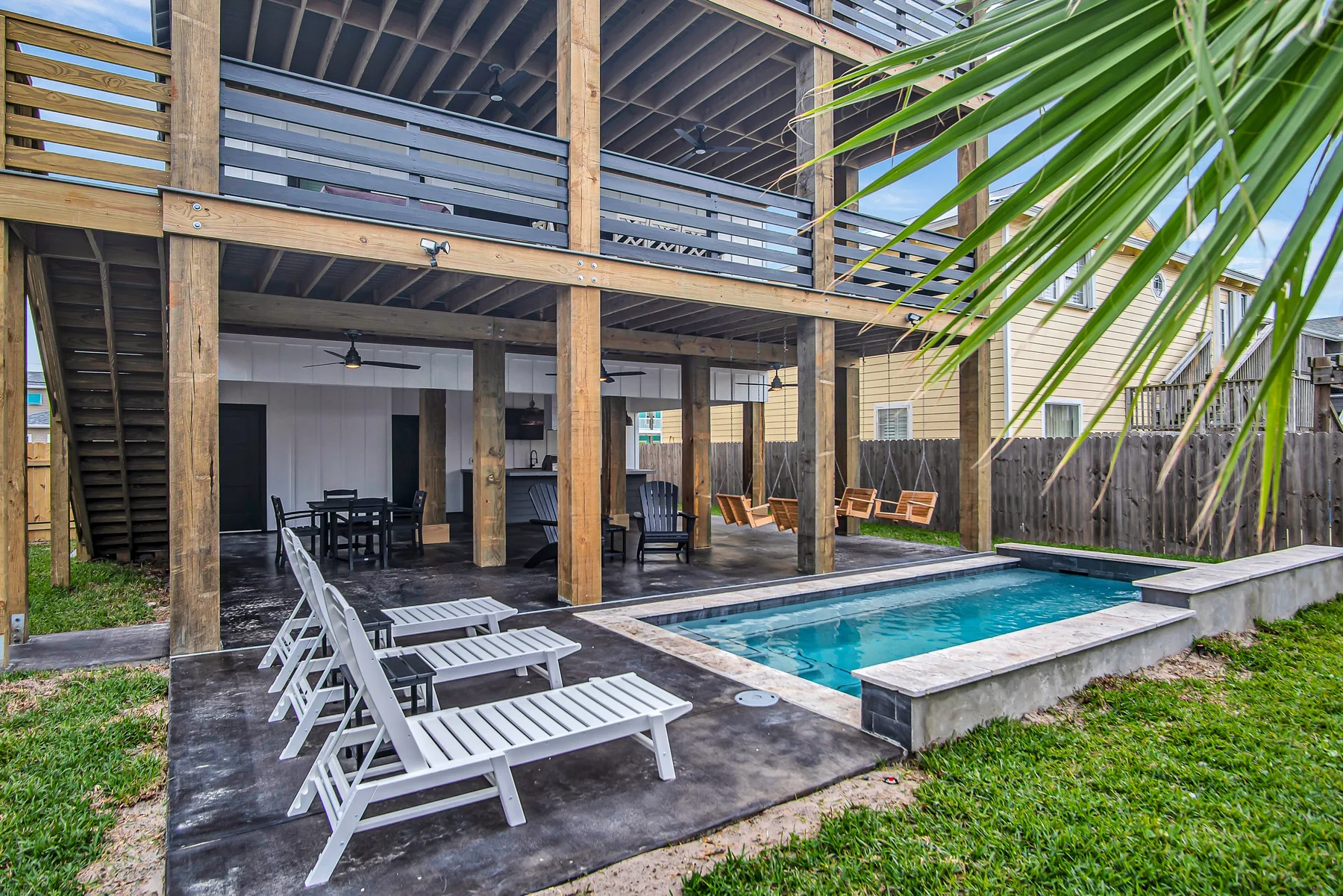 Una piscina al aire libre junto a una terraza de madera con asientos y un edificio abierto.