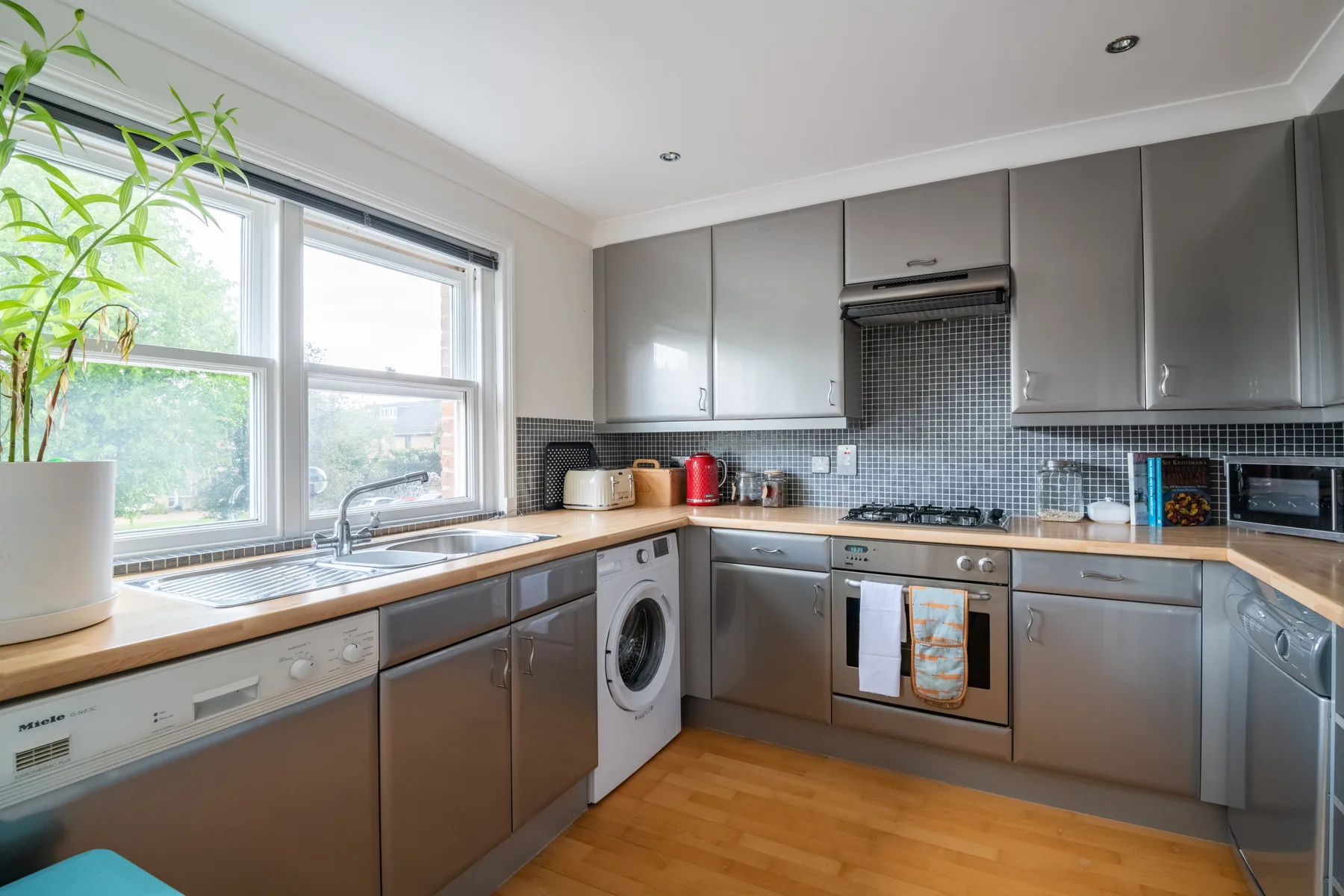 A modern kitchen with gray cabinets, a washing machine, and large windows.