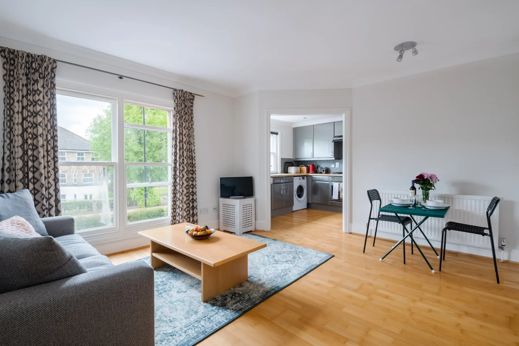 A bright living area opens onto a kitchen, with a dining table beside the window.