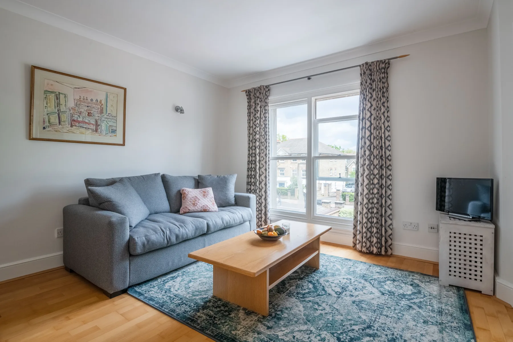 A bright living room with a gray sofa beside large curtained windows.