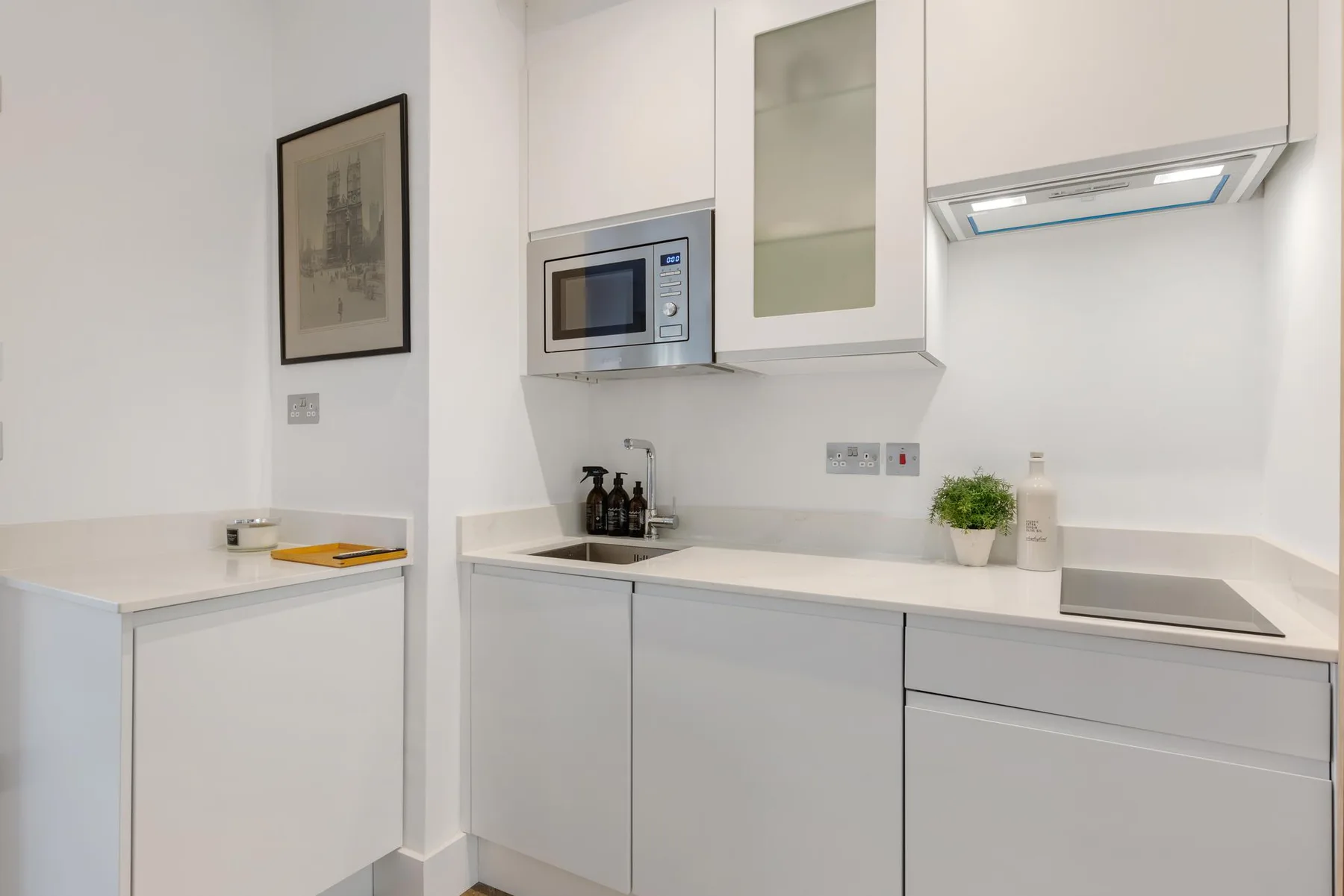Una cocina moderna y luminosa con armarios blancos, microondas y placa de cocina.