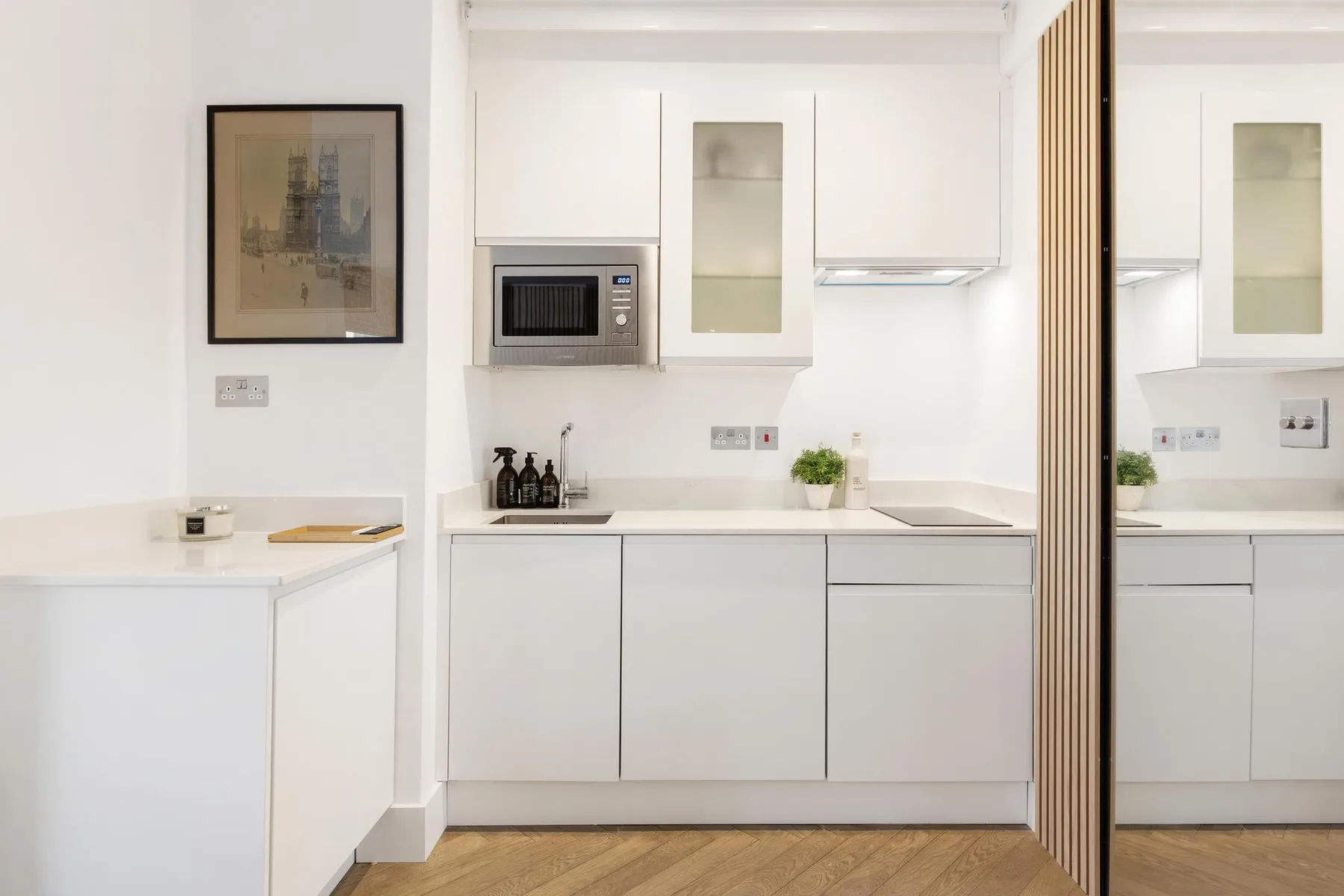 Una cocina moderna y luminosa con armarios blancos, encimera y suelo de madera.