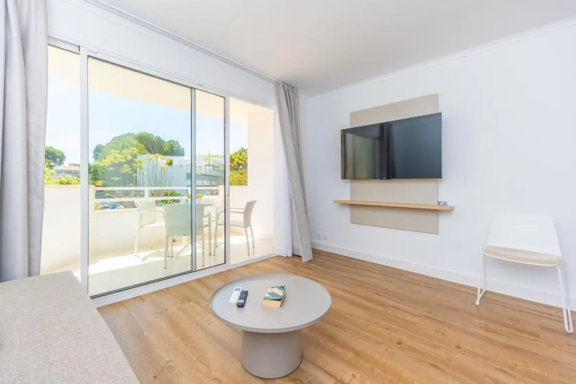 A bright living room with a wall-mounted television and sliding glass doors opening to a balcony.