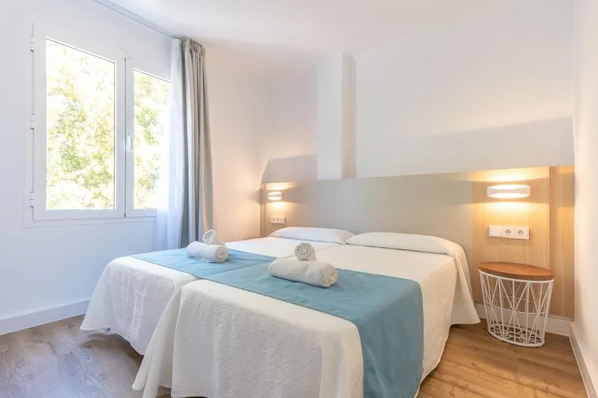 Bedroom with two beds, blue runners, bedside lights, and a window.