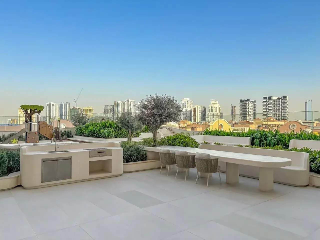 Una terraza en la azotea con una mesa larga al aire libre y edificios de la ciudad al fondo.