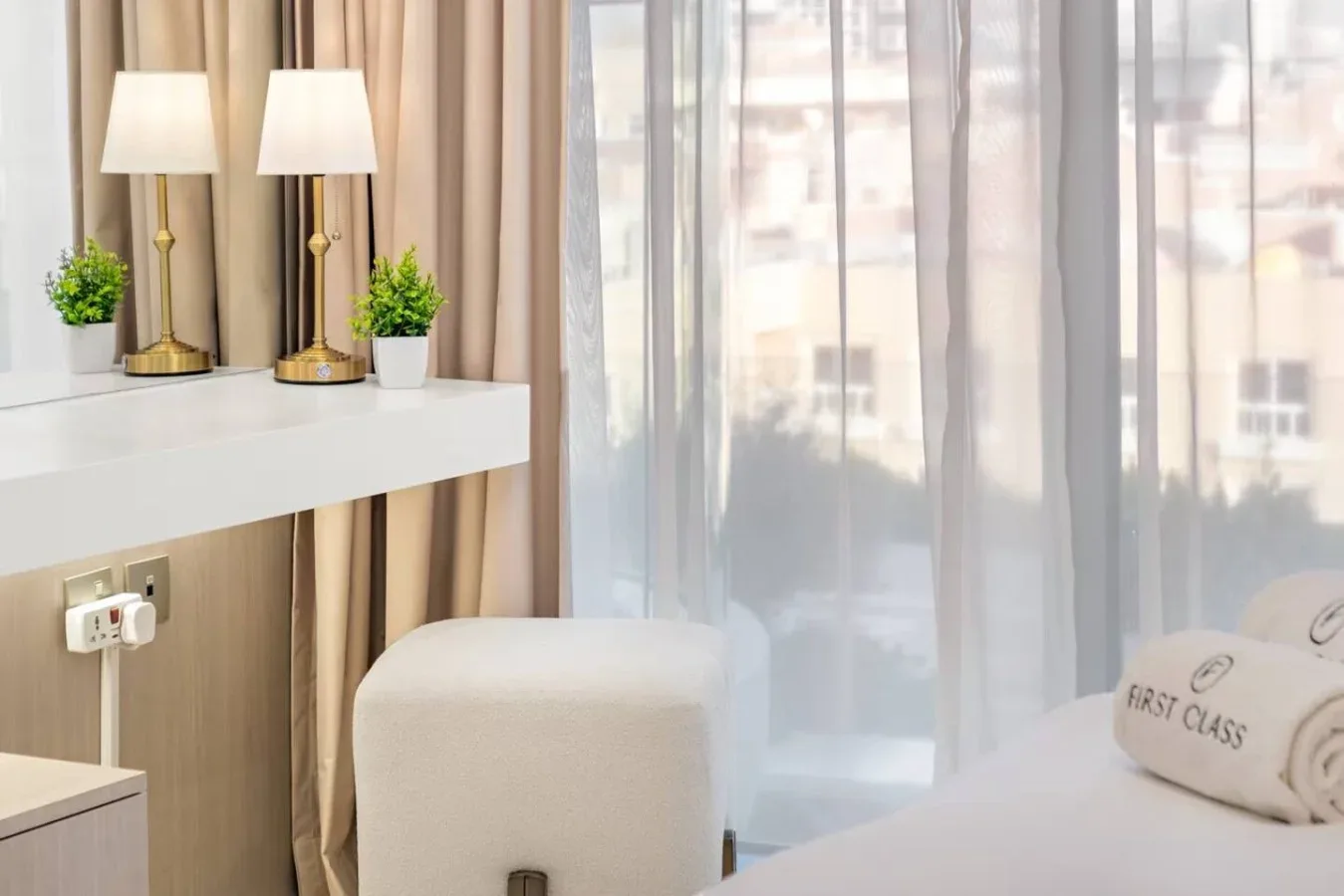 Un rincón de dormitorio con una mesa auxiliar, lámparas y cortinas traslúcidas.