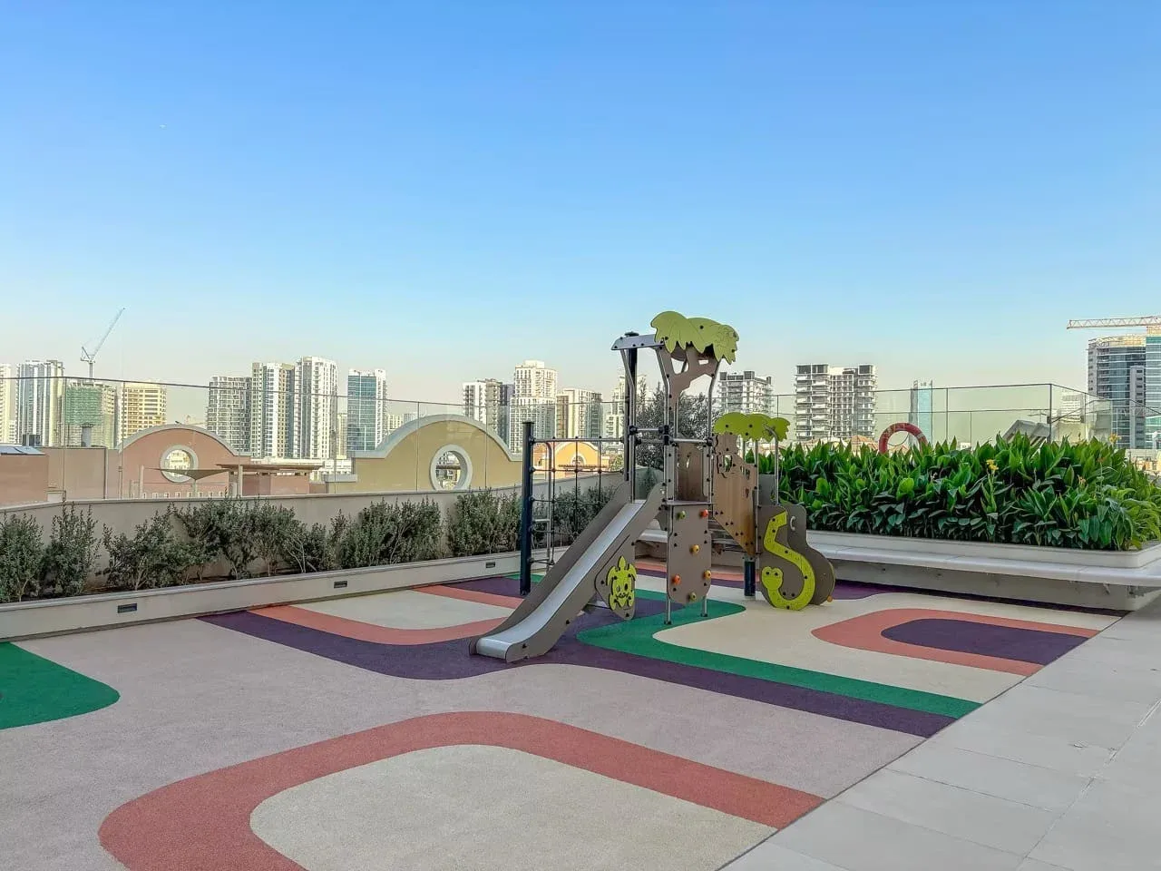 Un parque infantil en una azotea, con suelo de colores y edificios al fondo.