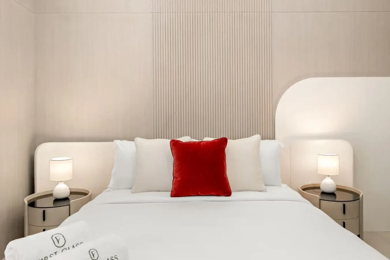 Una cama de dormitorio bien tendida, con ropa de cama blanca y un cojín rojo.
