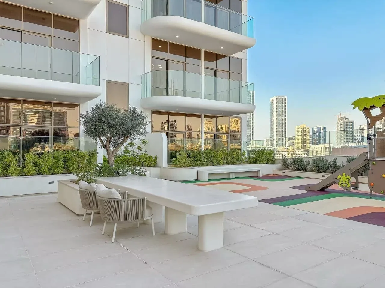 Una terraza en la azotea tiene una mesa larga al aire libre, asientos y una zona de juegos infantil.