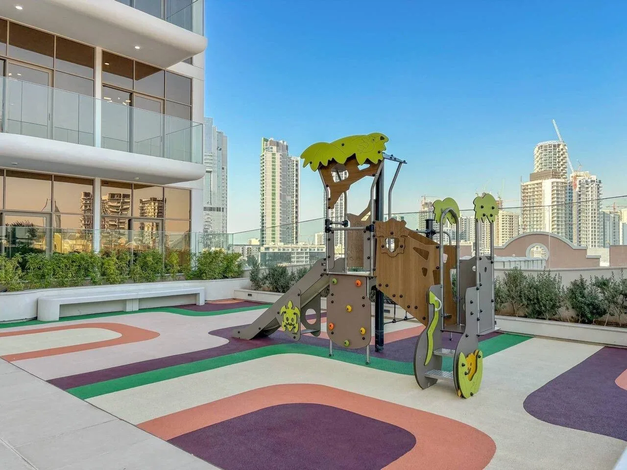 Un parque infantil en una azotea, con suelo de colores y edificios de la ciudad al fondo.