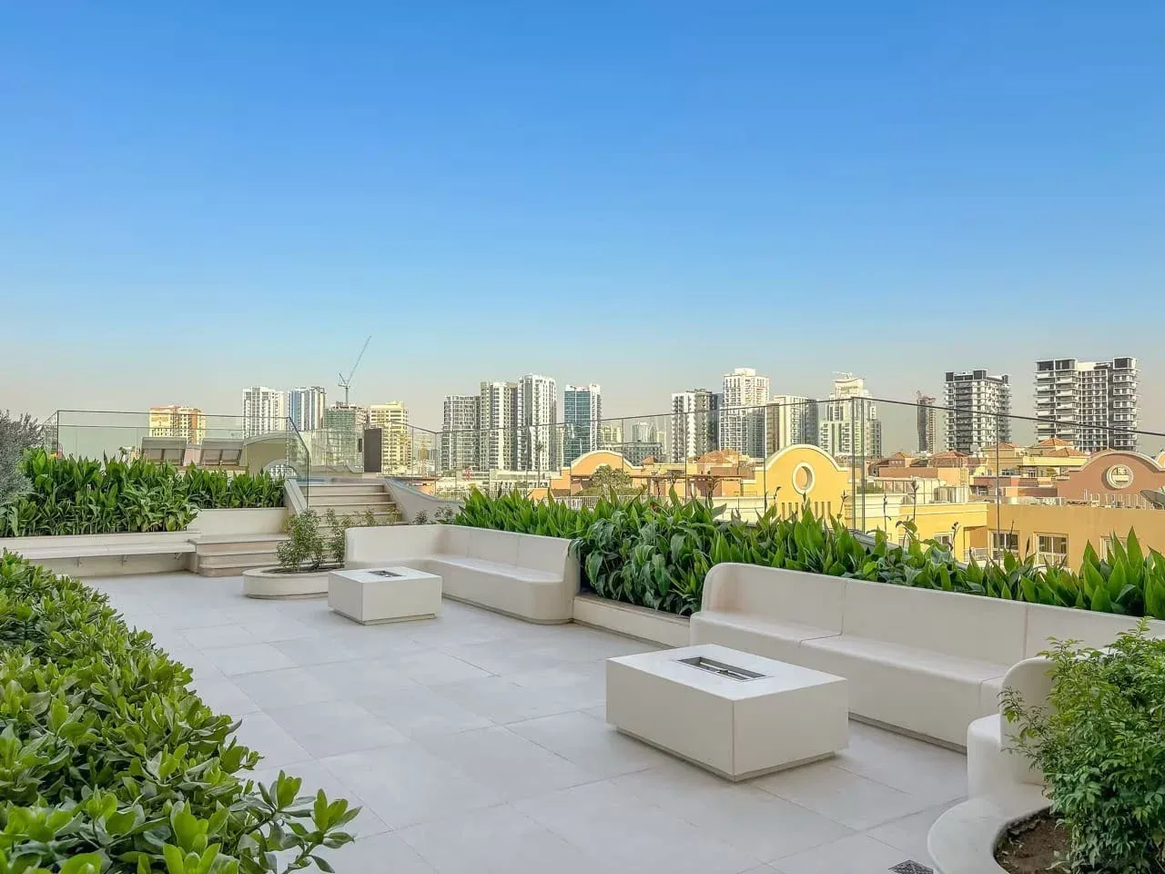 Una terraza en la azotea con suelo de baldosas, jardineras y vistas al horizonte urbano.