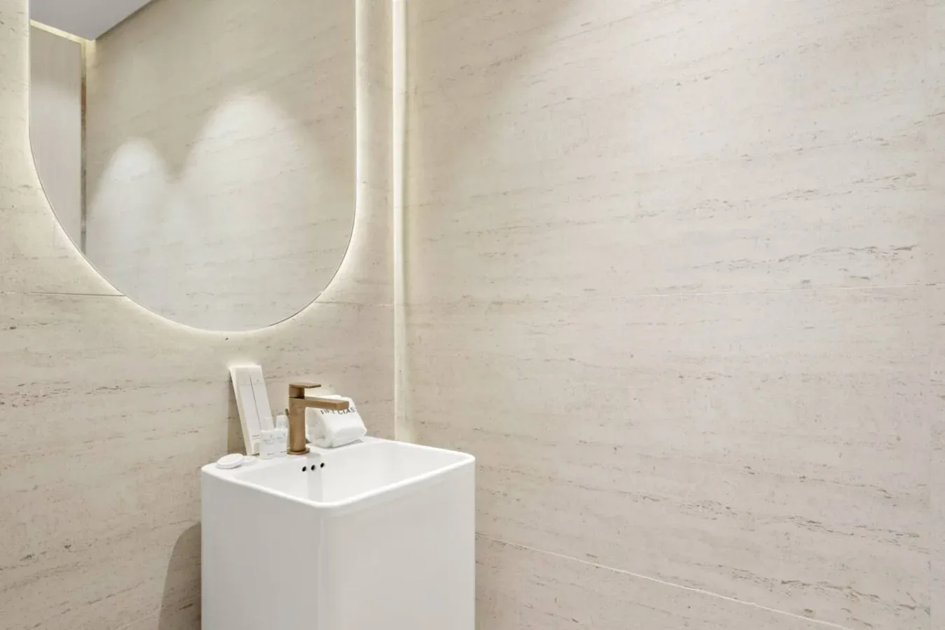 Un lavabo de baño está bajo un gran espejo redondeado, frente a paredes claras.