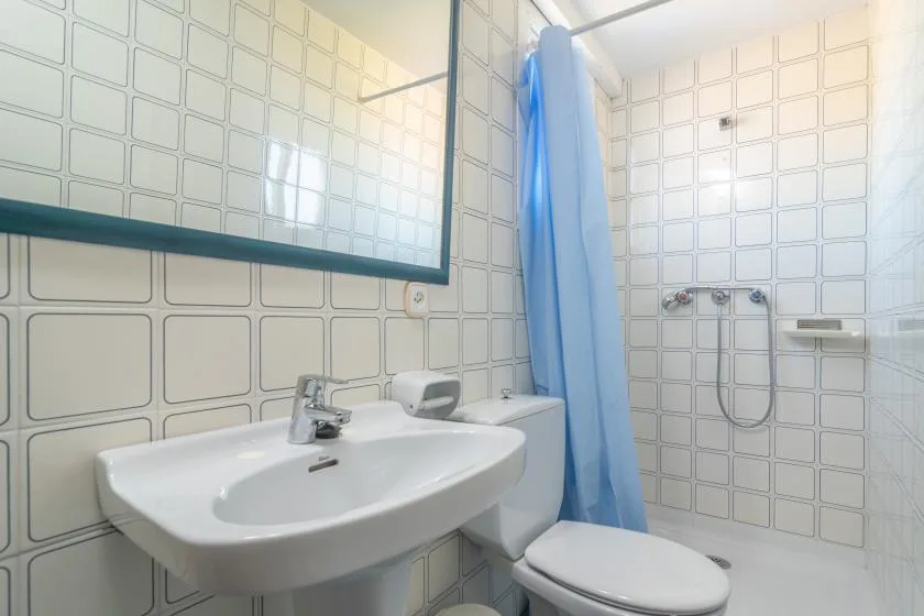 A tiled bathroom with a sink, toilet, and blue shower curtain.