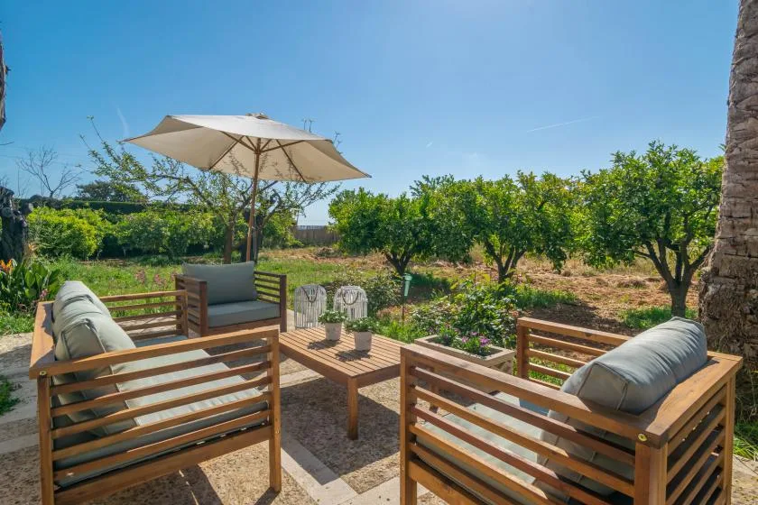 An outdoor patio with wooden seating, a sun umbrella, and a leafy garden.