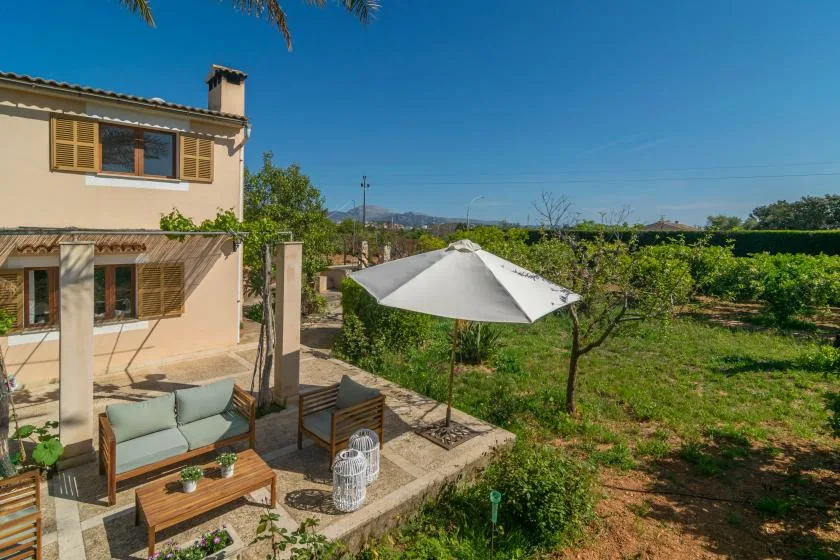 A patio with outdoor seating and a white umbrella overlooks a green garden.