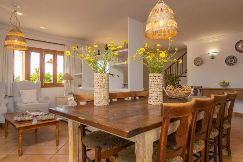 A dining area with a large wooden table, chairs, and yellow flowers.