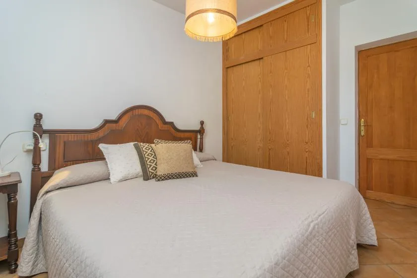 A bedroom with a large bed, decorative wooden headboard, and built-in wooden cupboards.