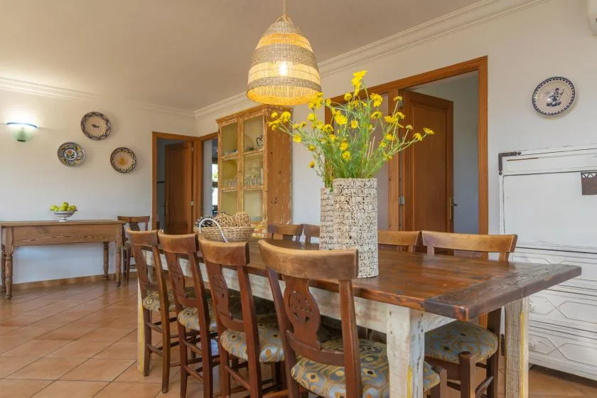 A dining room with a long wooden table and yellow flowers in a vase.