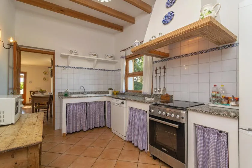 A tiled kitchen with a stove, countertop, and wooden ceiling beams.