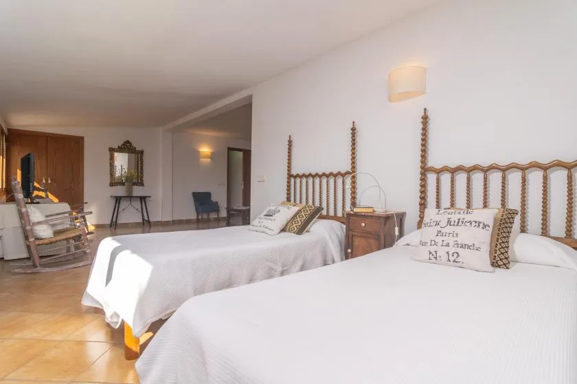 A bedroom with two beds, wooden headboards, and a chair.