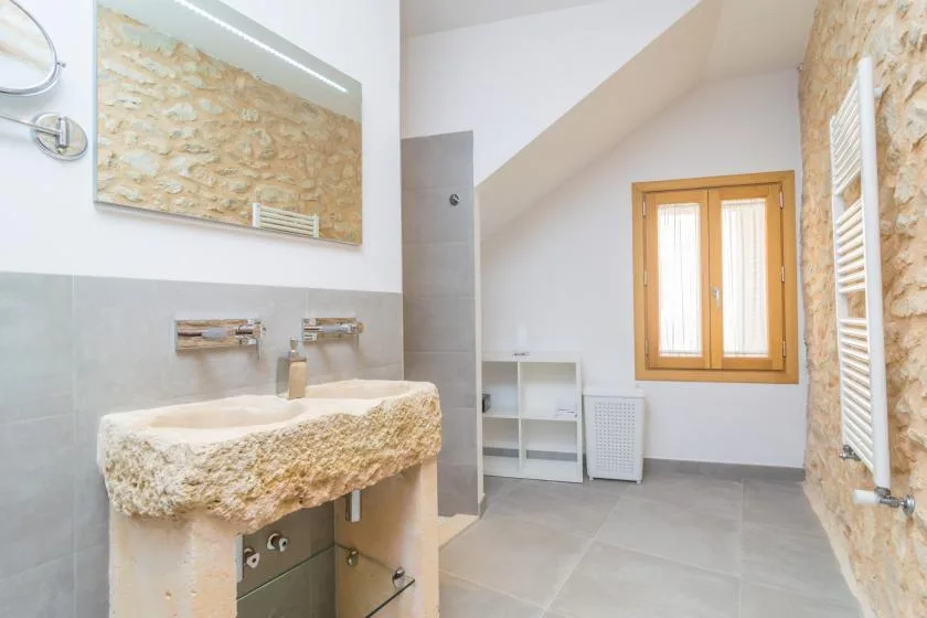 Un baño luminoso con un lavabo de piedra y una ventana con marco de madera.